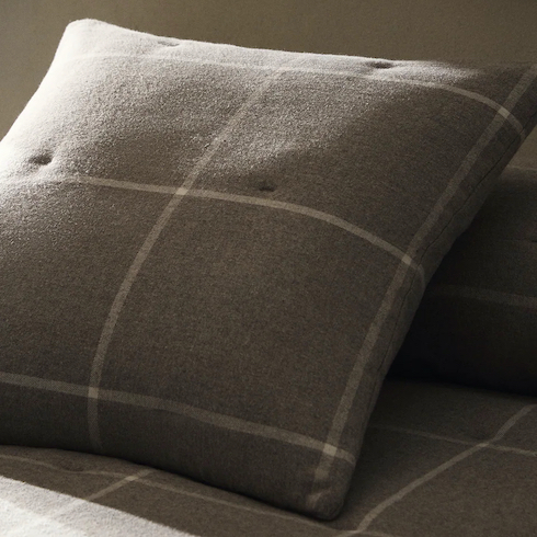 Grey and white flannel throw pillow cover with a check print on a bed in a darkened room