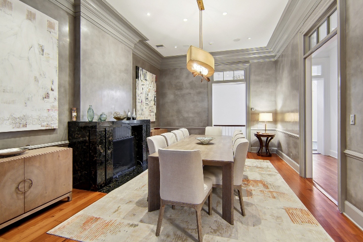 A formal dining room with table, chairs, pendant light overhead, large windows and a marble fireplace.
