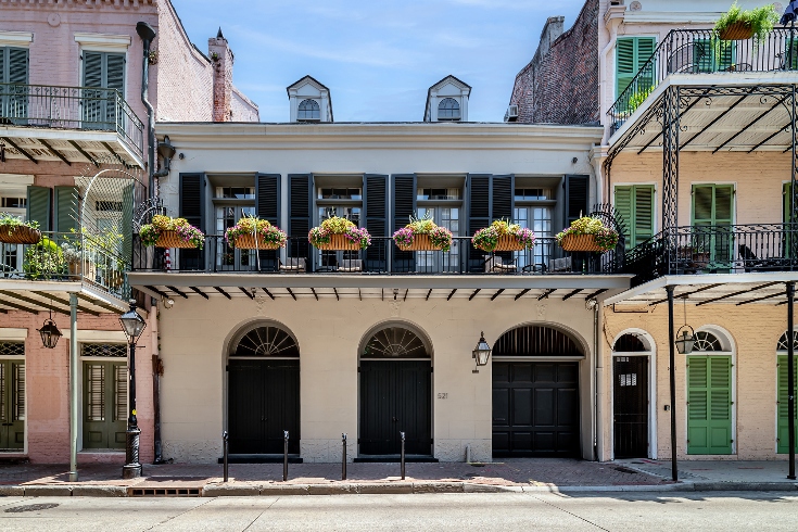 The front of an 1830s Parisian-style New Orleans French Quarter mansion with French doors and a herringbone sidewalk. 