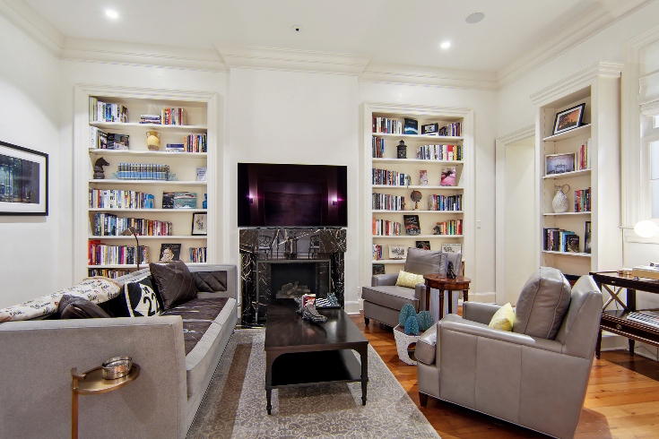A home library with marble fireplace, a sofa and armchairs and custom display shelves on each wall.