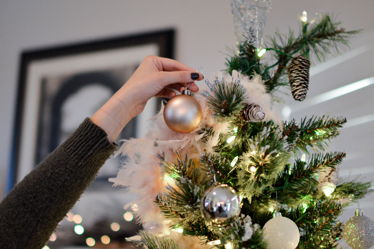A hand hangs a Christmas bauble on a tree with white string lights