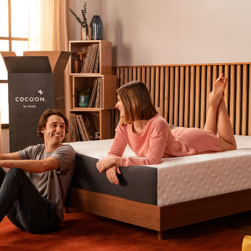 A young. couple lounges on a bed with a brand new mattress