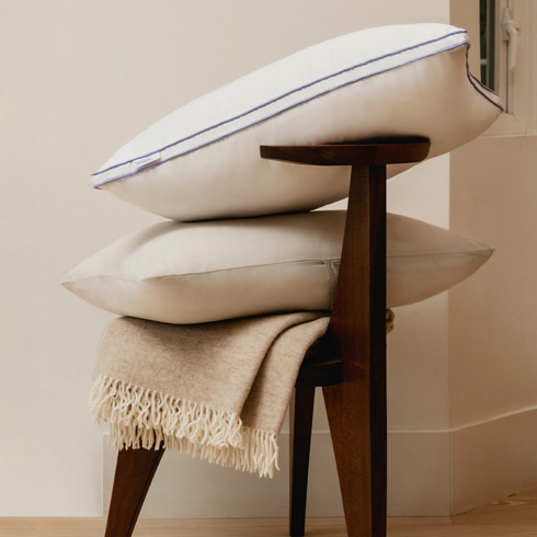 White pillows stacked on a wood chair on top of a throw blanket