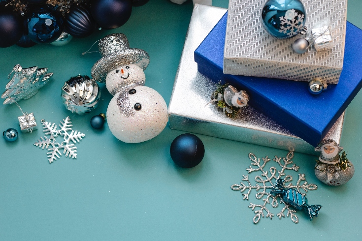 Three gifts wrapped in blue and silver on a light blue background and a few ornaments scattered about.