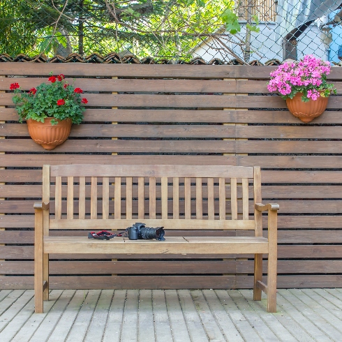 A deck with a wooden fence, a wooden bench and two hanging plants.