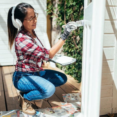 A woman wearing headphones and painting a home exterior