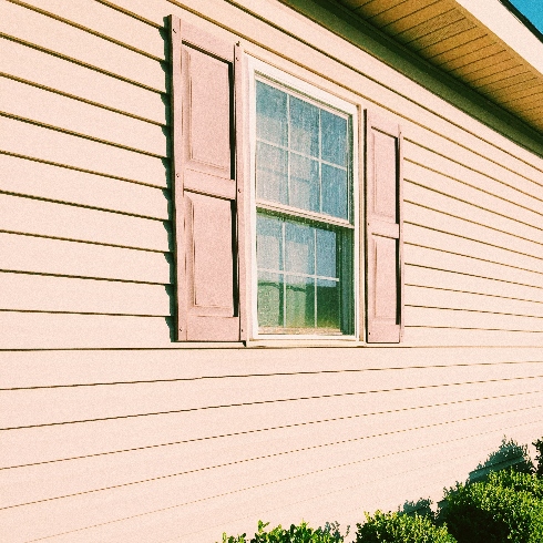A home with sandy pink-toned siding and a window with shutters