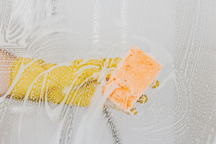 A yellow glove holding and orange sponge in how to clean grout in the shower