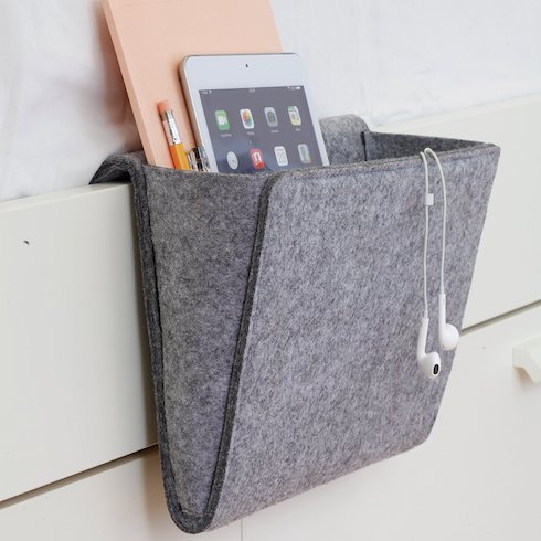 Kikkerland Felt Bedside Caddy from Well.ca hangs off the edge of a white bed and is filled with an iPage, pencils and a peach coloured notebook