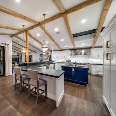 Celebrity homes - Midcentury-style house owned by celebrities Emily Blunt and John Krasinski in the Hollywood Hills featuring a stunning kitchen with high wooden beams, a blue kitchen island and wide plank wood floors