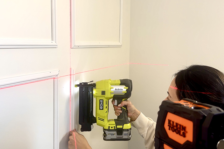 Courtney Ryall using a laser level and brad nailer to secure the moulding.