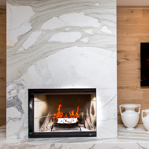 White marble fireplace with large surround seat with two white urns and a wooden wall behind