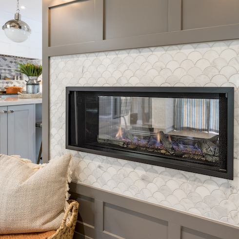 See-through gas fireplace with white scallop tiles and brown panelling divides the kitchen and the dining room in a remodelled home featured on HGTV Canada