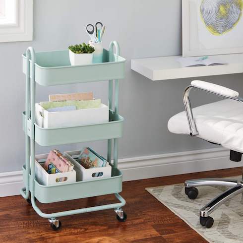 Mint green Type A Momentum Steel 3-Tier Utility Cart from Canadian Tire filled with art supplies sits on a wood floor next to a white desk and office chair on a white patterned rug