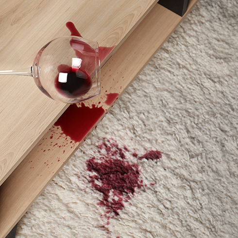 Overturned glass and spilled red wine on white carpet indoors, above view