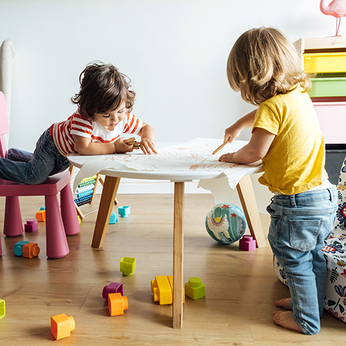 Side view preschool kids playing drawing in modern table with small armchair while spending time together in playroom of modern kindergarten. Children learning concept