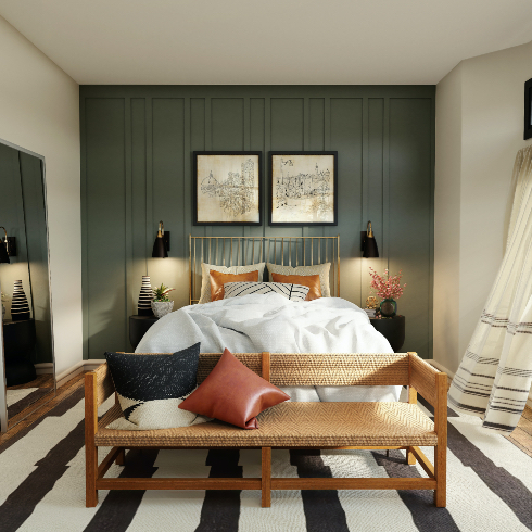 A gold framed bed against a dramatic steel blue accent wall in a chic bedroom with a wood and cane bench seat, black and white striped rug, two black and gold wall scones, two black bedside drum tables, two black framed drawings above the bed, black and white curtains, and a large wall mirror