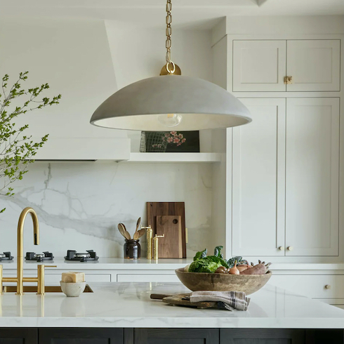 Elliot Pendant by Light House featured in HGTV Canada’s kitchen lights gallery in a modern kitchen with a large centre island with a sink, soap bowl, and a large stone bowl filled with vegetable, marble countertops and backsplash, white cabinets and large stove fan hood, gold hardware, cutting boards, grinders and a spoon pot on the counter