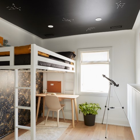 Children's bedroom with loft bed and star constellations on ceiling, a wooden desk and chair, a potted plant, wood floors, a small white rug, a window with roman blinds, and a telescope on a stand