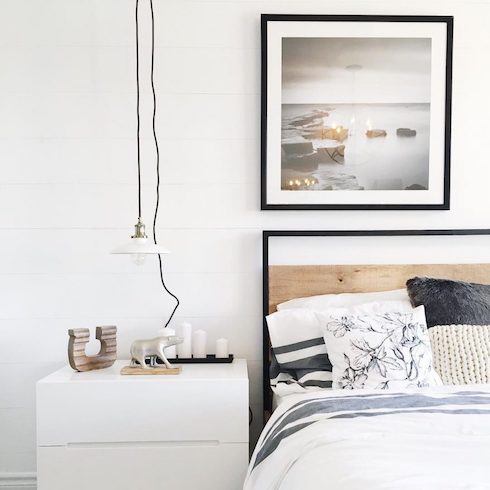 Chic black and white bedroom designed by Ottawa-based Leclair Décor featuring a black framed bed, black framed wall art, a white bedside table with a polar bear statue, a tray of white candles and a white pendant lamp with a black cord.