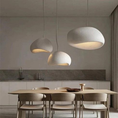 Three Khmara Wabi-Sabi Pendant Lights featured in HGTV Canada’s kitchen lights gallery shown in a chic kitchen with brown and white stone countertops and backsplash, ash wood cabinets, a cutting board with bread and a rolling pin, two wooden stools, and under cabinet lighting