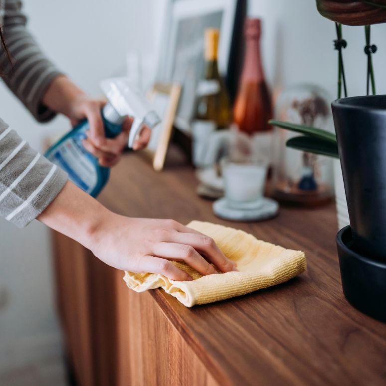 person cleaning wooden counter with cloth and cleaning solution