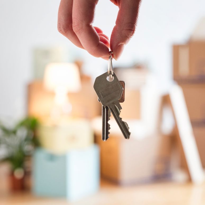 Person holding keys in new home with moving boxed blurred in distance
