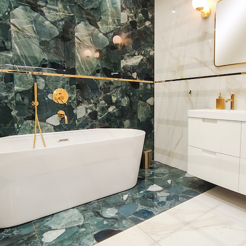 Bathroom interior with white standalone bathtub, floating vanity and sink, cream coloured ceramic tile walls, statement stone splash wall, and gold hardware shown in the HGTV Canada gallery Unusual Bathroom Renovation Ideas That Will Be Popular In 2025