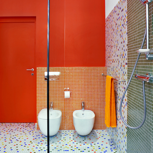 Colourful bathroom with white and multicoloured tile floor, red wall, white bidet and toilet, and a metal towel rack with an orange towel shown in the HGTV Canada gallery Unusual Bathroom Renovation Ideas That Will Be Popular In 2025