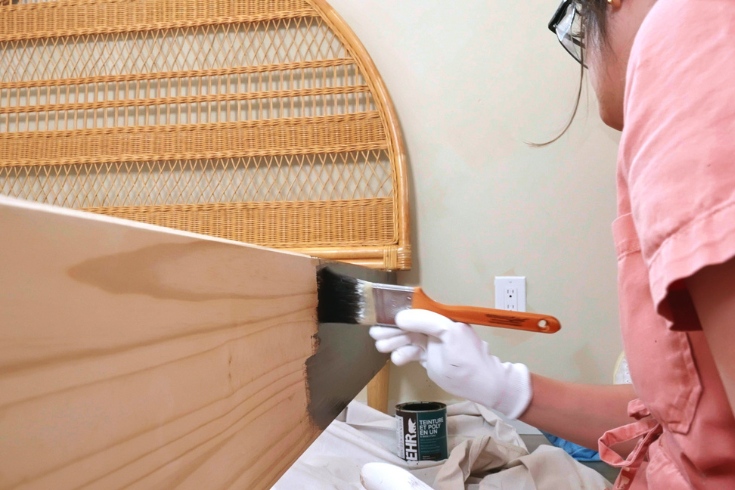 Person painting bed with stain