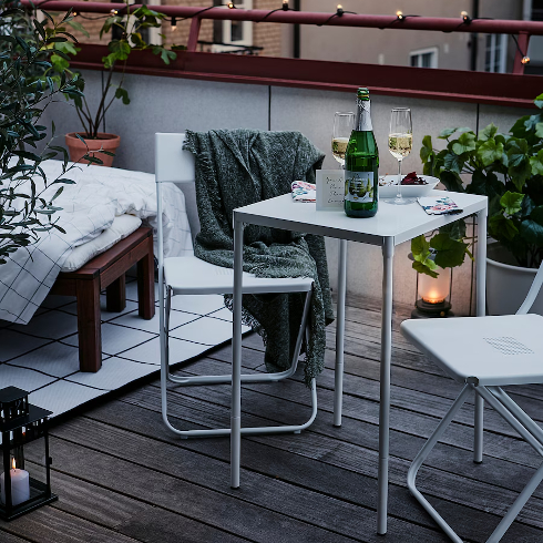 The white metal Fejan table from IKEA holds a bottle of wine and glass on a cozy patio