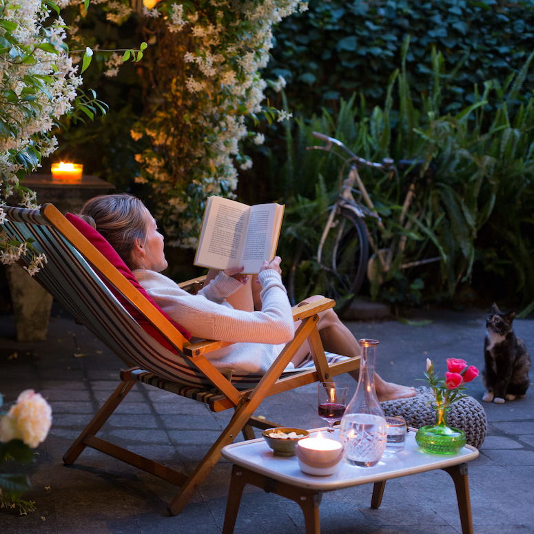 Woman relaxing on deck chair in a no-grass backyard, reading a book with her cat watching as featured in HGTV.ca's The Best Ways to Pull Off a No-Grass Backyard