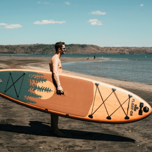 A man holding his paddle board next to a large body of water