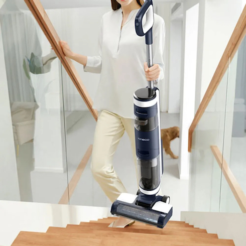 Woman walking up wooden stairs with a glass railing holding a Tineco Wet Dry vacuum as part of How to Get Rid of Dust From Every Type of Surface at Home for HGTV.ca