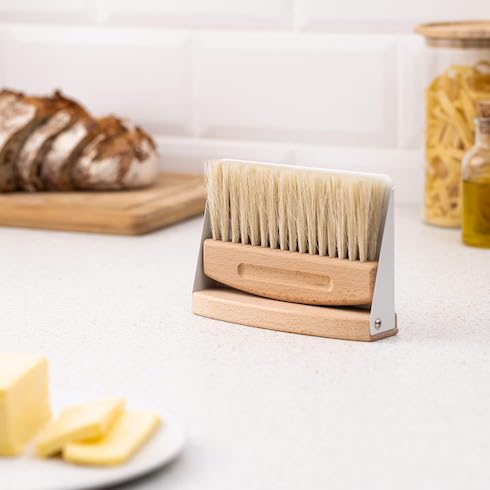 Navaris Small Dustpan and Brush Set sits on top of a white kitchen counter with a breadboard and pasts jars in the background and a white plate with sliced butter as part of How to Get Rid of Dust From Every Type of Surface at Home for HGTV.ca