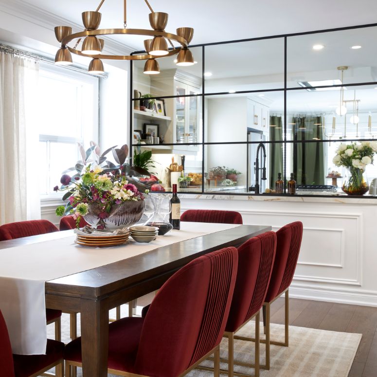 Mirror next to sleek and bright dining room table with red velvet chairs