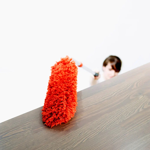 A woman uses an OXO Microfiber Extendable Duster on the top of a dark wooden shelf as part of How to Get Rid of Dust From Every Type of Surface at Home for HGTV.ca