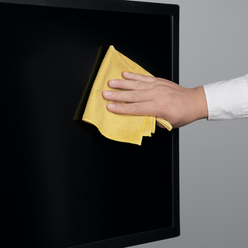 A hand uses a yellow Ikea Pepprig Microfibre cloth to white a black TV screen as part of How to Get Rid of Dust From Every Type of Surface at Home for HGTV.ca