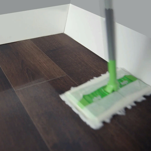 A blurry Swiffer Sweeper 2-in-1 Dry + Wet Floor Mop cleans a dark wood floor next to white baseboards as part of How to Get Rid of Dust From Every Type of Surface at Home for HGTV.ca