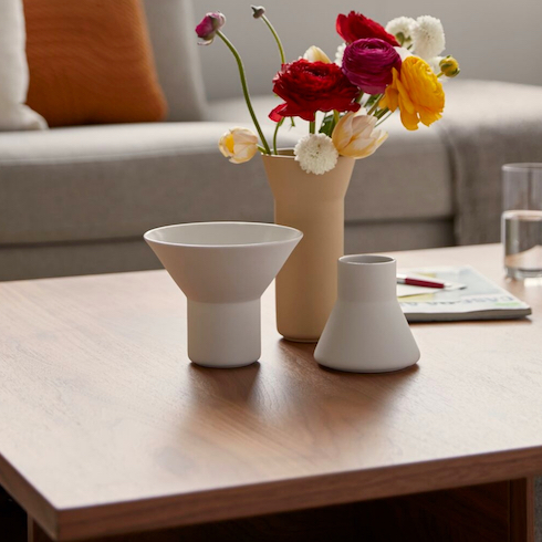 Three ceramic Alfred vessels by Winnipeg-based designer Carla Zacharias for EQ3 sit on a coffee table with flowers, a pen and paper, and a glass of water with a couch in the background as part of HGTV Canada's 10 Gift Ideas for the Men in Your Life