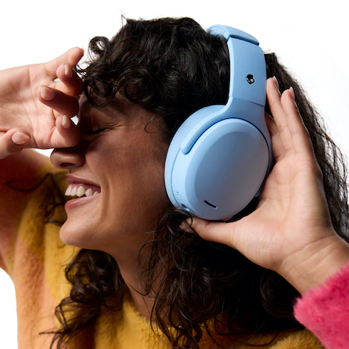 A woman with dark curly hair wearing a yellow sweater listens to blue Skullcandy Crusher ANC 2 Sensory Bass Headphones with Active Noise Canceling as part of HGTV's 10 Gift Ideas for the Women in Your Life