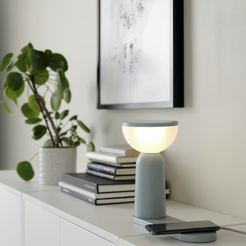 Ikea's BETTORP LED mobile lamp sits on a credenza with a stack of books, a potted plant, and framed print on the wallas part of HGTV's 10 Gift Ideas for the Women in Your Life