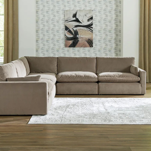 Cloud couch dupes featuring Ashley Home Store's Sophie 5 Piece Modular Sectional sitting in a living room with oak floors, a white rug, wallpaper on the wall behind with hung art and tall chartreuse drapes