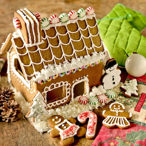 A festive gingerbread house with candy and cookie decorations surrounding it.