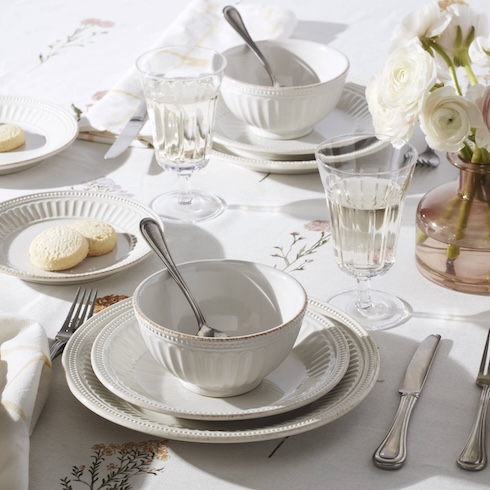 Two table settings, each with white plates and a matching bowl, are on an elegant tablescape.