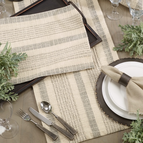 A rustic striped table runner and matching dinnerware sit on a wood table.